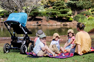 Mum with four children and pram sitting on a picnic rug overlooking the water.