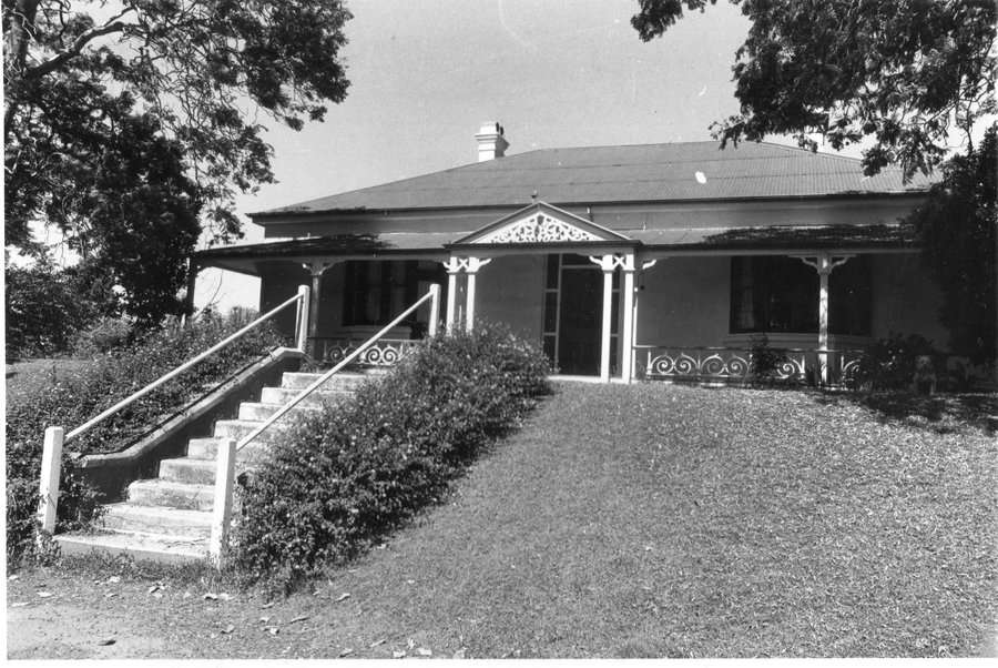 Black and white photo of Fernside home. Single-story with stairs leading up to entry, surrounded by large trees.