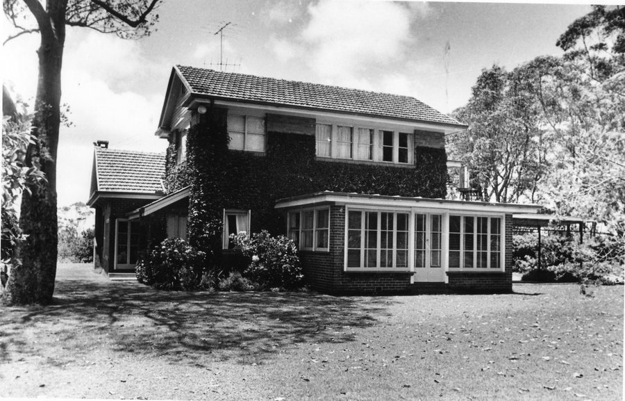 Black and white photo of Boyce Gardens residence. Brick double-story home surrounded by gardens and large trees.