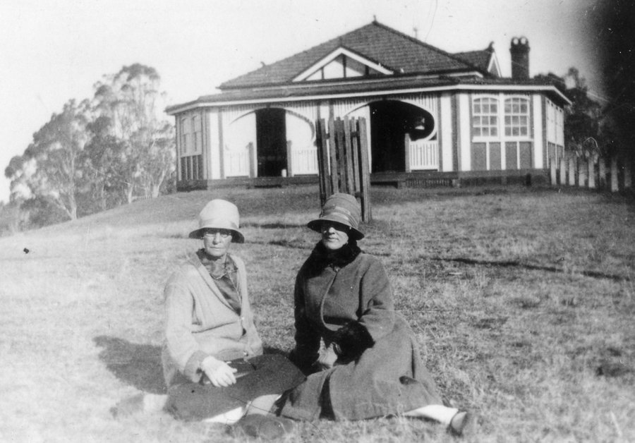Historical black and white photo of Picnic Point kiosk in 1935. Two ladies sitting on grass in front of kiosk.