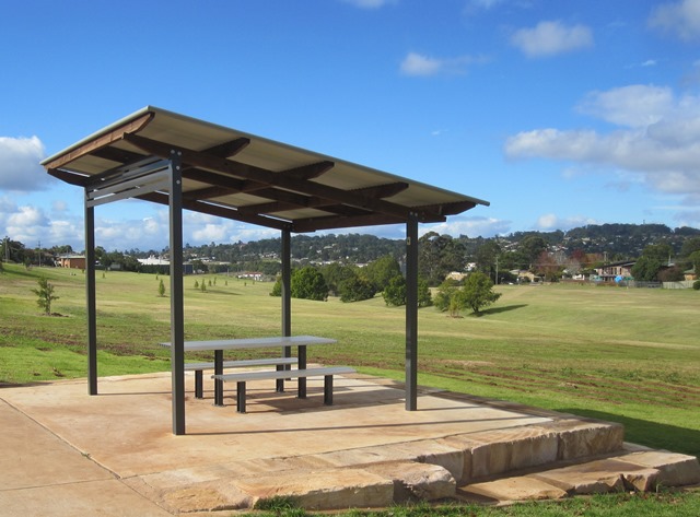 Black Gully picnic shelter covering one picnic table and surrounded by open green grassy space.