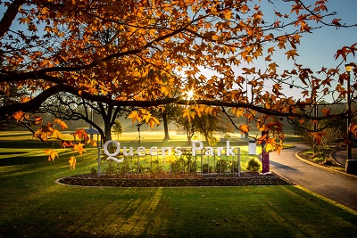 Queens Park Entry signage. Beautiful golden sunlight peaking through the autumn leaves.