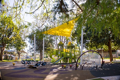 Queens Park Lindsay Street playground. Modern play equipment shaded by beautiful leafy green trees.
