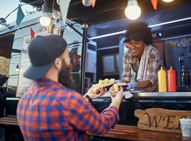 Lady serving food to a customer from a food truck. The lady has a big smile on her face.